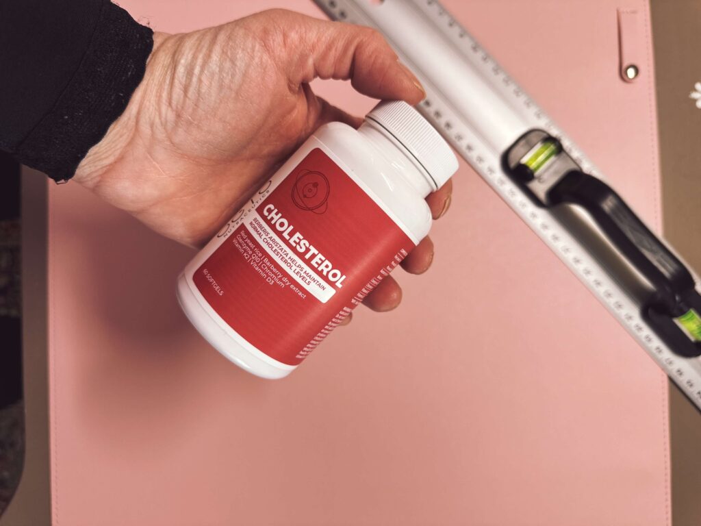 Hand hält eine Dose mit Cholesterin-Supplementen auf pinkem Hintergrund, im Fokus steht das Produktetikett. Cholesterin-Supplement in der Hand gehalten – Unterstützung für den Fettstoffwechsel.