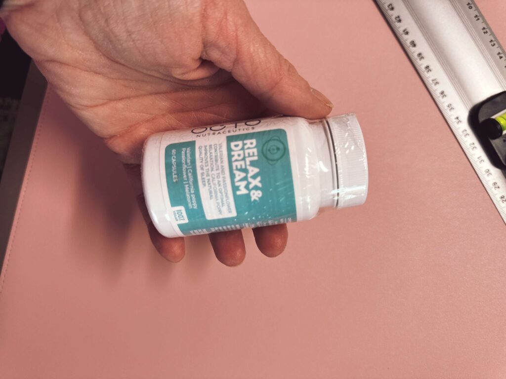 Hand hält eine weiße Dose mit Schlaf- und Entspannungs-Supplementen auf pinkem Hintergrund, das Produkt ist noch versiegelt. Relax & Dream – Schlaf- und Entspannungssupplement für eine bessere Nachtruhe.